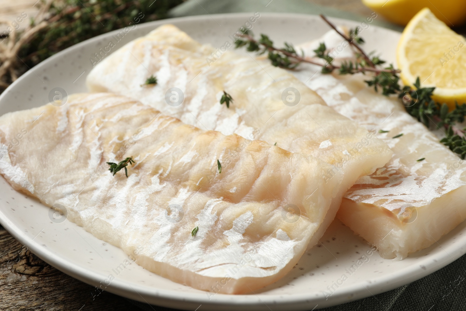Photo of Fresh raw cod fillets with thyme and lemon on wooden table, closeup