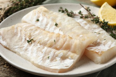Fresh raw cod fillets with thyme and lemon on wooden table, closeup