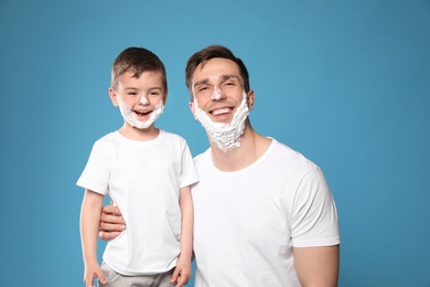 Photo of Funny dad and his little son with shaving foam on faces against color background
