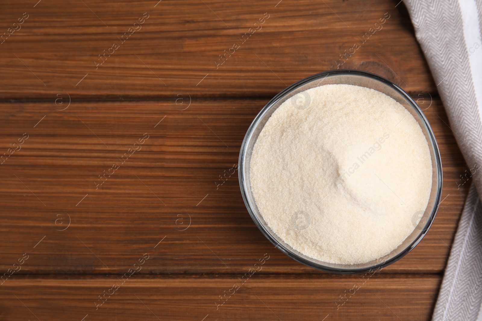 Photo of Gelatin powder in glass bowl on wooden table, top view. Space for text