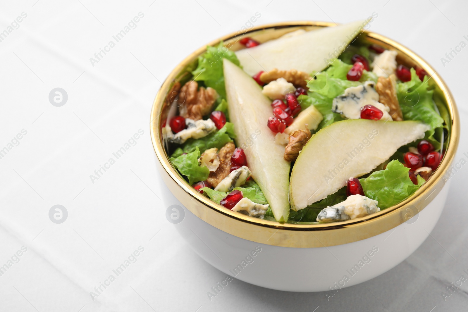 Photo of Delicious pear salad in bowl on light tiled table, closeup. Space for text