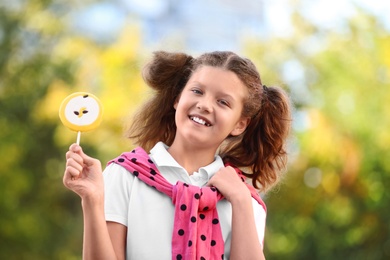 Photo of Cute little girl with tasty candy outdoors