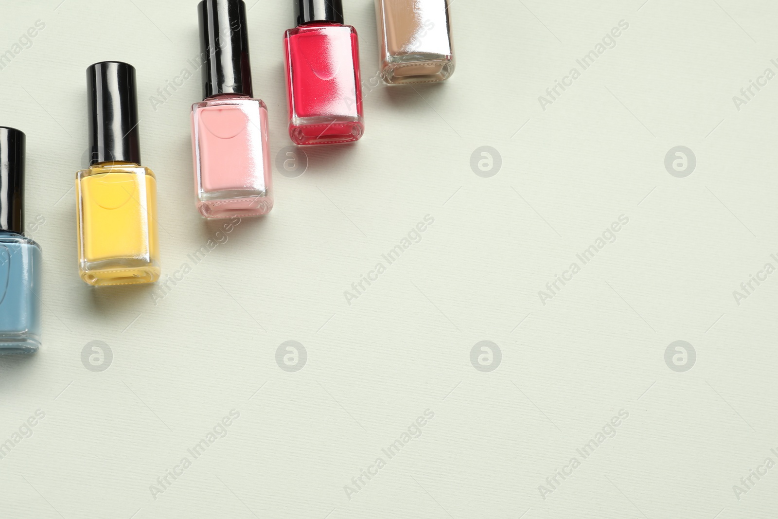 Photo of Colorful nail polishes in bottles on light background, flat lay. Space for text