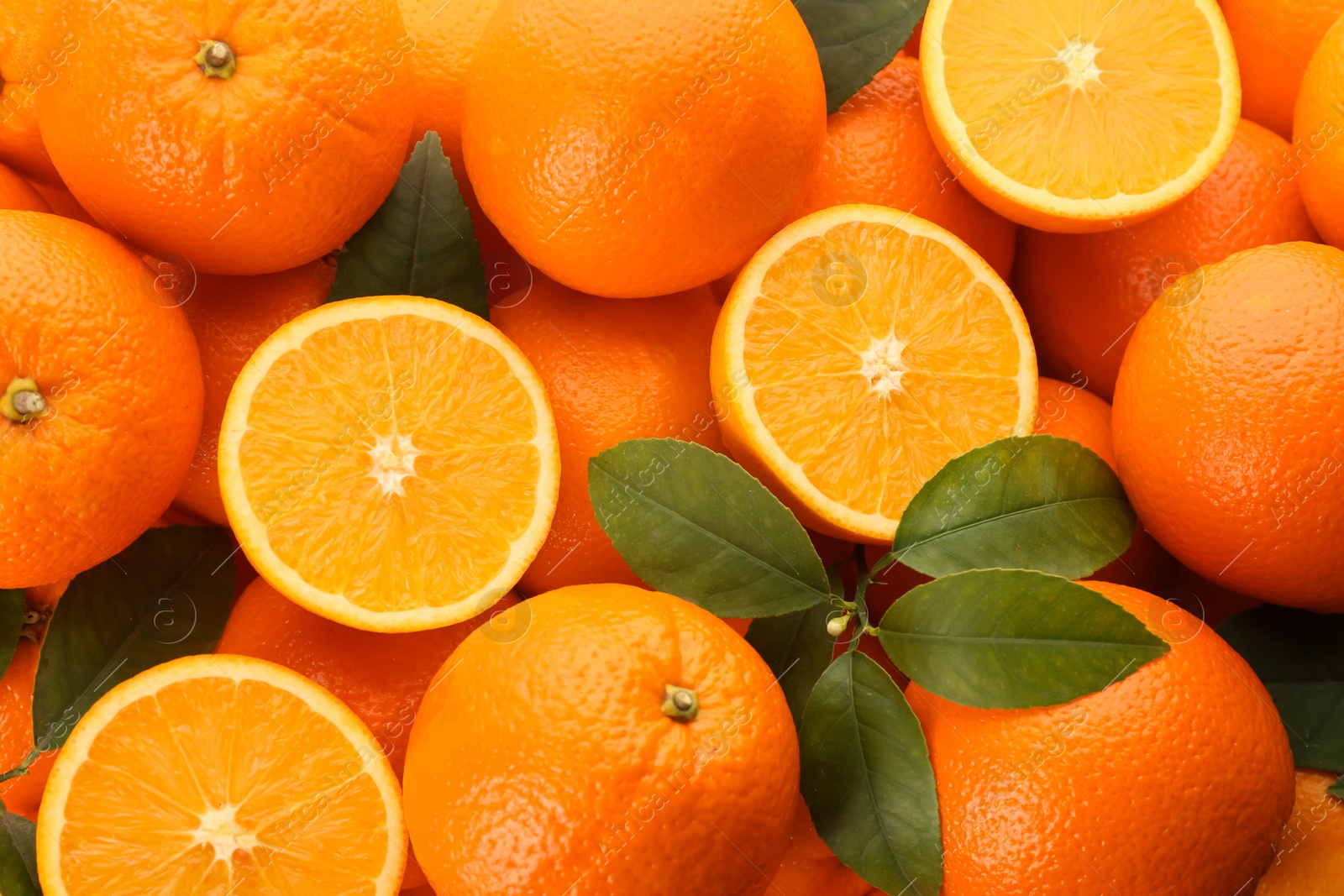 Photo of Cut and whole fresh ripe oranges with green leaves as background, top view