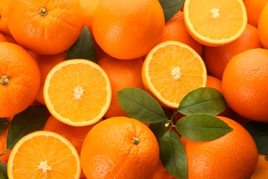 Cut and whole fresh ripe oranges with green leaves as background, top view