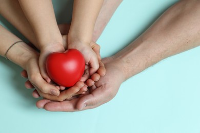 Parents and child holding red decorative heart on light blue background, top view