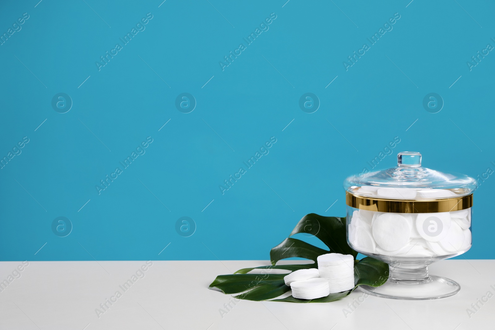 Photo of Jar with cotton pads on white table against blue background. Space for text