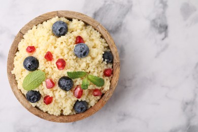 Photo of Bowl of tasty couscous with blueberries, pomegranate and mint on white marble table, top view. Space for text