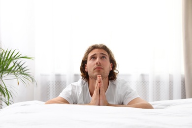 Handsome young man saying bedtime prayer at home