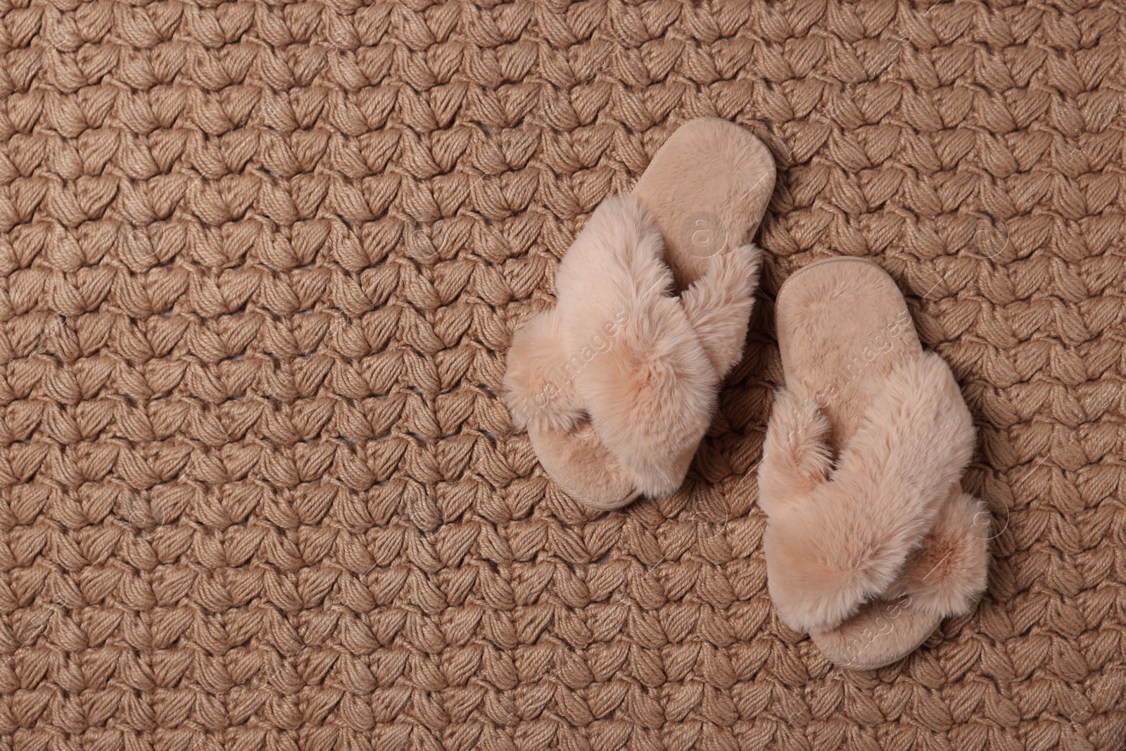 Photo of Fluffy beige slippers on soft carpet, top view. Space for text