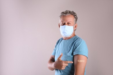 Photo of Senior man in protective mask pointing at arm with bandage after vaccination on beige background. Space for text