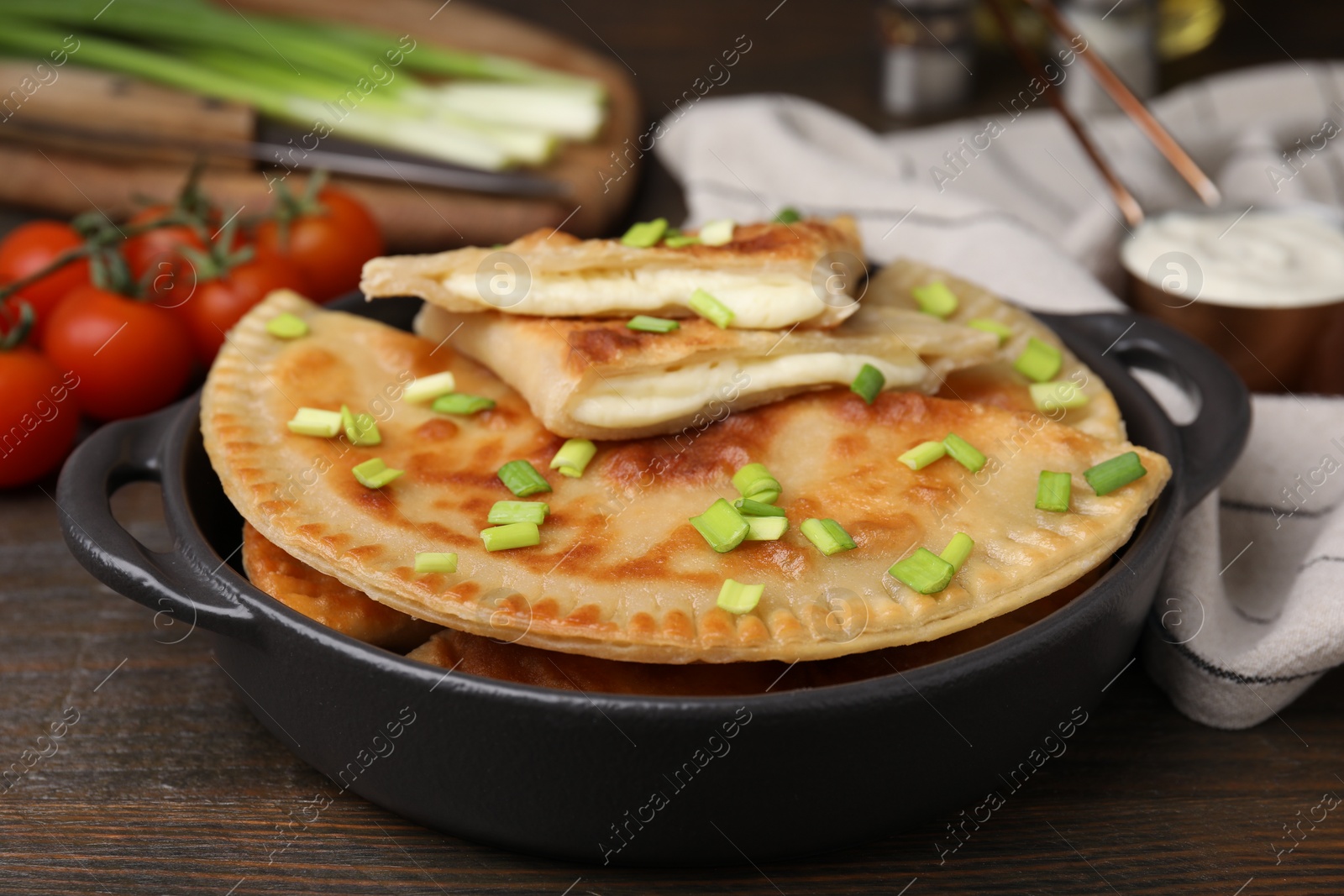 Photo of Delicious fried chebureki with cheese and green onion on wooden table