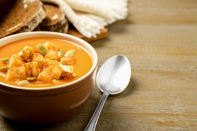 Photo of Tasty creamy pumpkin soup with croutons and seeds in bowl on wooden table. Space for text