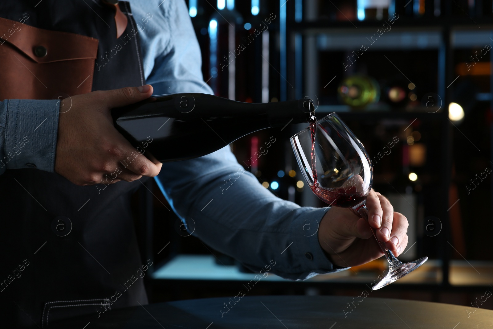 Photo of Bartender pouring red wine from bottle into glass indoors, closeup