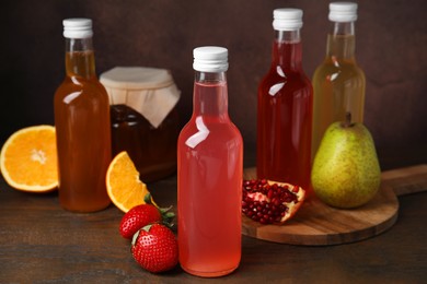 Photo of Delicious kombucha in glass bottles, jar and fresh fruits on wooden table