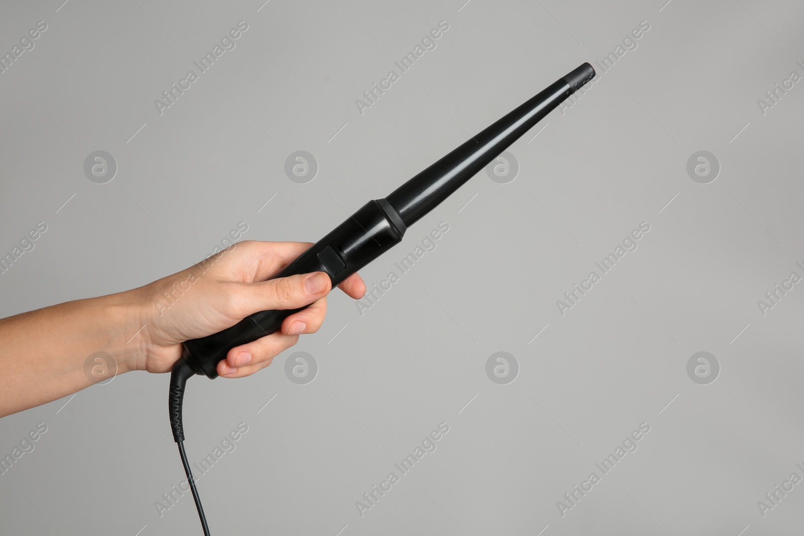Photo of Woman holding clipless curling hair iron on light grey background, closeup