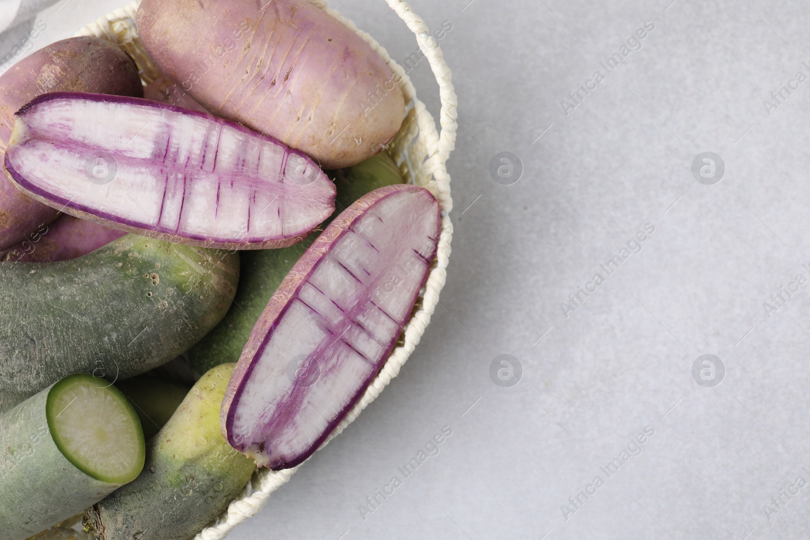 Photo of Purple and green daikon radishes in wicker basket on light grey table, top view. Space for text