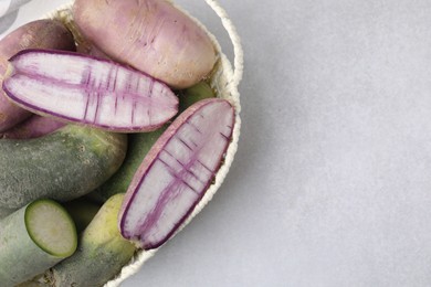 Purple and green daikon radishes in wicker basket on light grey table, top view. Space for text