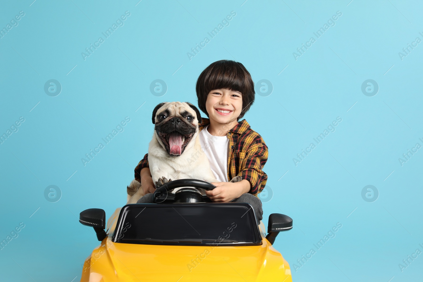 Photo of Little boy with his dog in toy car on light blue background