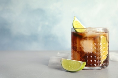 Glass of cocktail with cola, ice and cut lime on table. Space for text