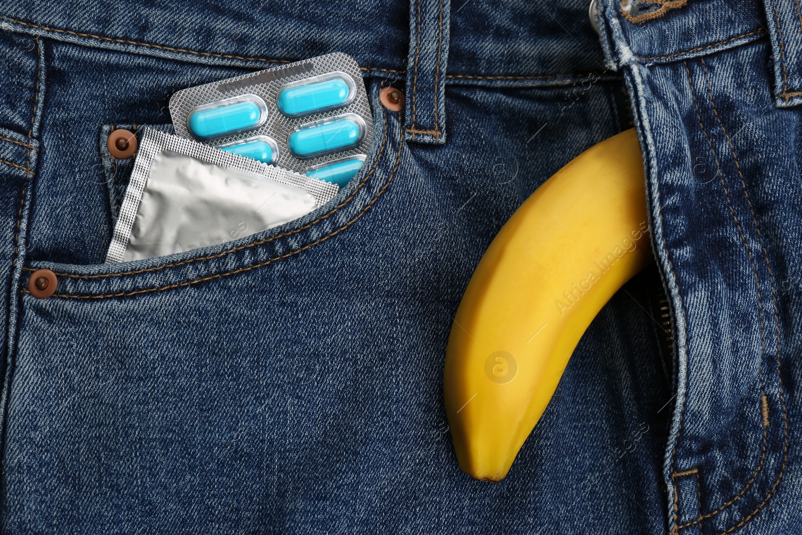 Photo of Banana symbolizing male sexual organ and pills with condom in jeans pocket, top view. Potency problem concept