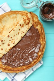 Photo of Tasty crepes with chocolate paste served on turquoise wooden table, flat lay