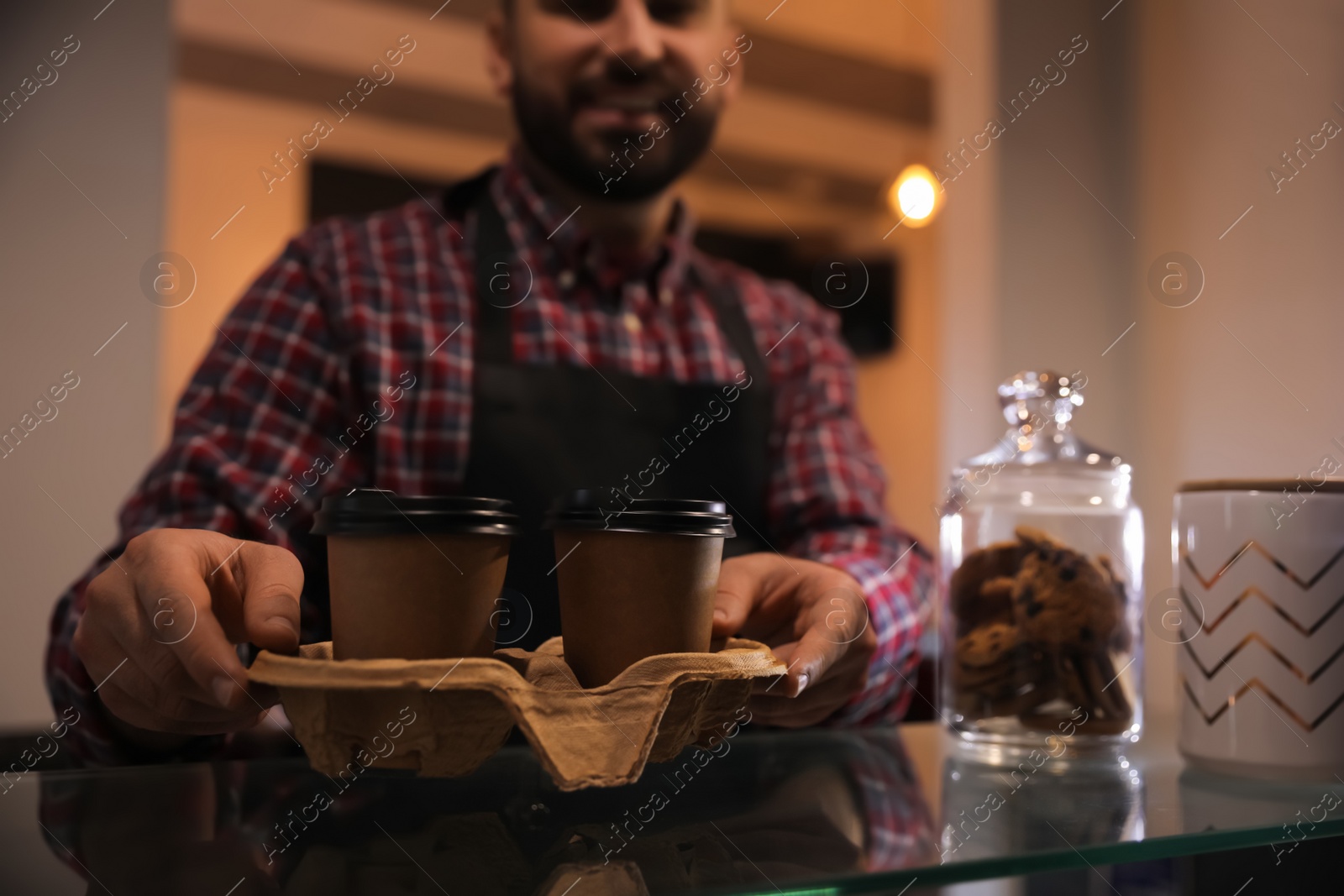 Photo of Barista putting takeaway coffee cups with cardboard holder on glass table in cafe, closeup