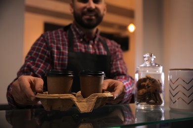 Photo of Barista putting takeaway coffee cups with cardboard holder on glass table in cafe, closeup