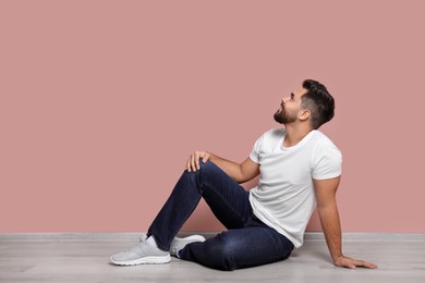 Photo of Young man sitting on floor near pink wall indoors. Space for text
