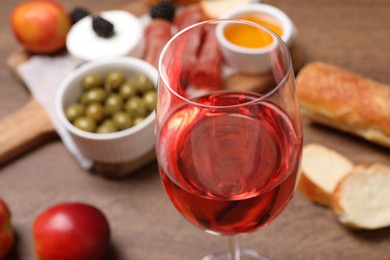 Photo of Glass of delicious rose wine and snacks on table, closeup