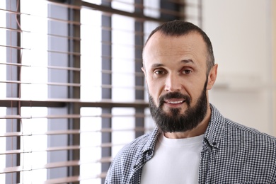 Photo of Portrait of handsome mature man near window with blinds indoors