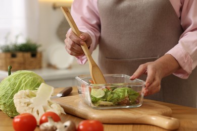 Woman cooking salad at wooden table in kitchen, closeup