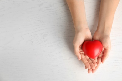 Photo of Woman holding red heart on wooden background, top view with space for text. Cardiology concept