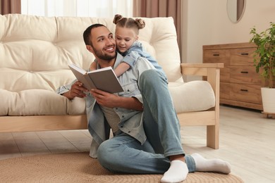 Photo of Little girl with her father reading book at home. International family