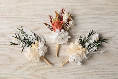 Stylish boutonnieres on white wooden table, flat lay