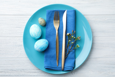 Festive Easter table setting with eggs and floral decoration on wooden background, flat lay