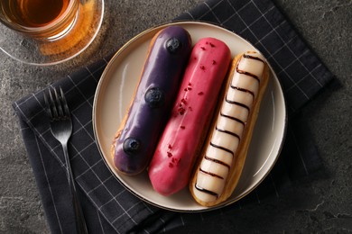 Photo of Different tasty glazed eclairs served with tea on grey textured table, flat lay