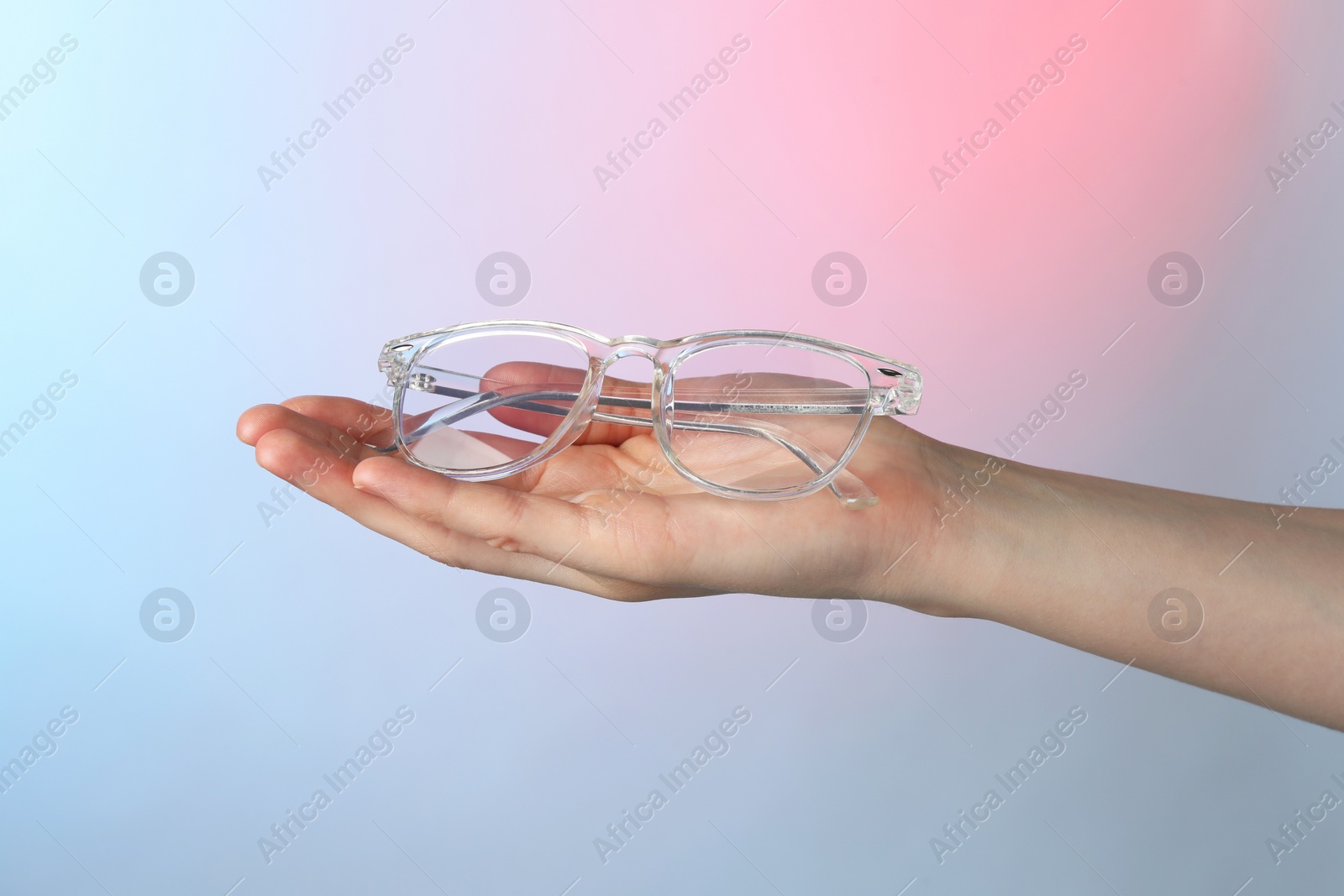 Photo of Woman holding glasses with transparent frame on color background, closeup
