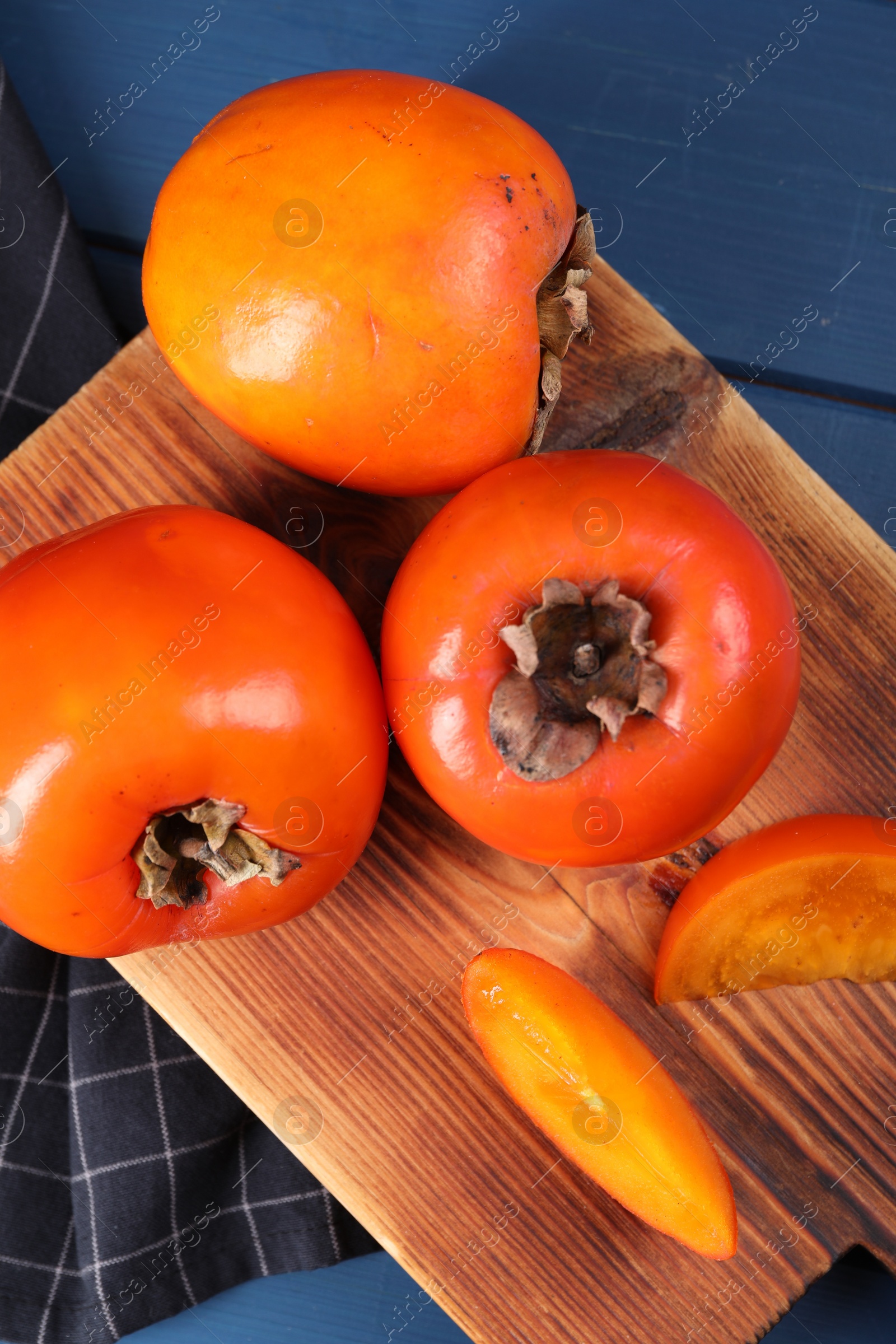 Photo of Delicious ripe persimmons on blue wooden table, top view