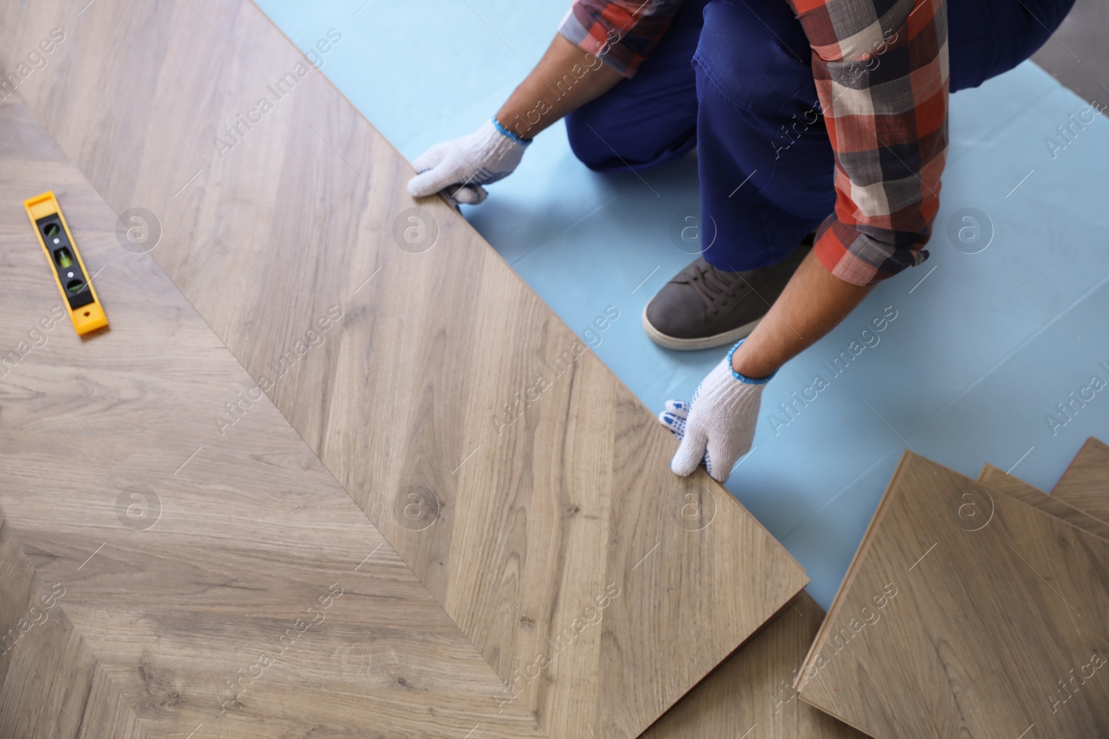 Photo of Worker installing laminated wooden floor indoors, closeup