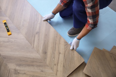 Photo of Worker installing laminated wooden floor indoors, closeup