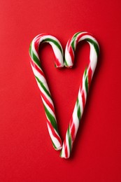 Photo of Heart made of Christmas candy canes on red background, flat lay