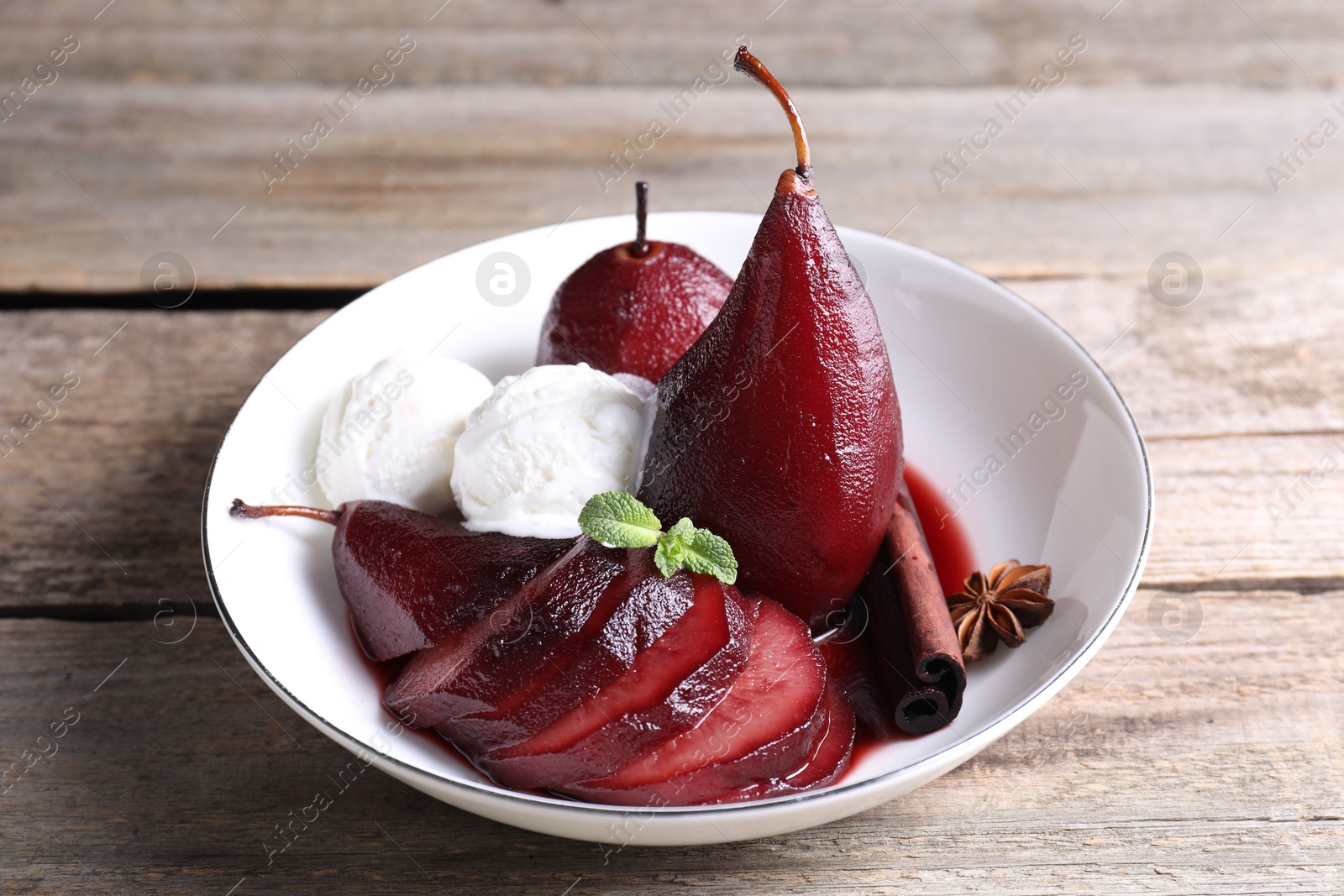 Photo of Tasty red wine poached pears and ice cream in bowl on wooden table, closeup