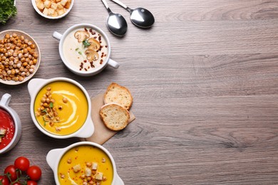 Photo of Different tasty cream soups and bread on wooden table, flat lay. Space for text