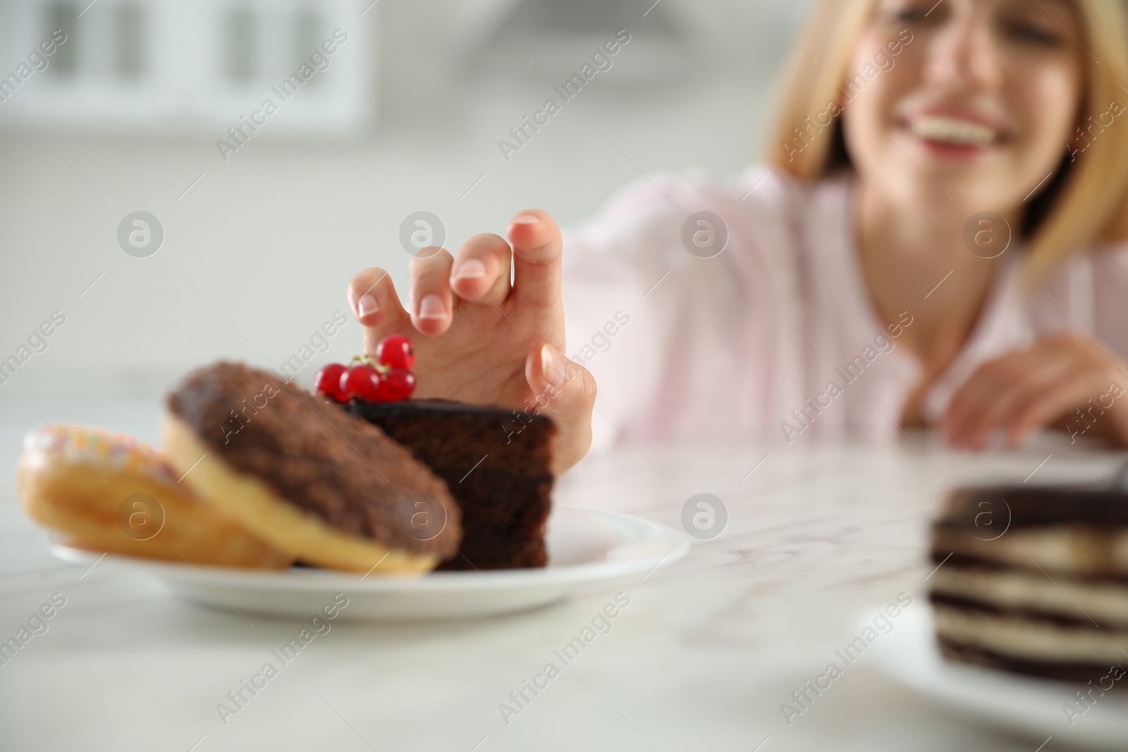 Photo of Concept of choice between healthy and junk food. Woman with sweets at white table in kitchen, focus on hand