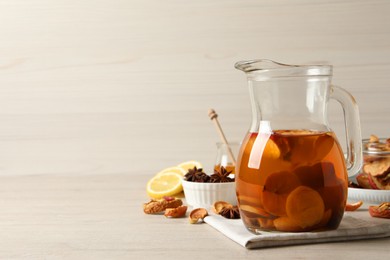 Delicious compote with dried fruits in glass jug on light wooden table, space for text