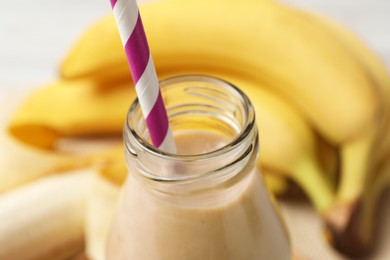 Photo of Bottle of tasty banana smoothie with straw and fresh fruits, closeup