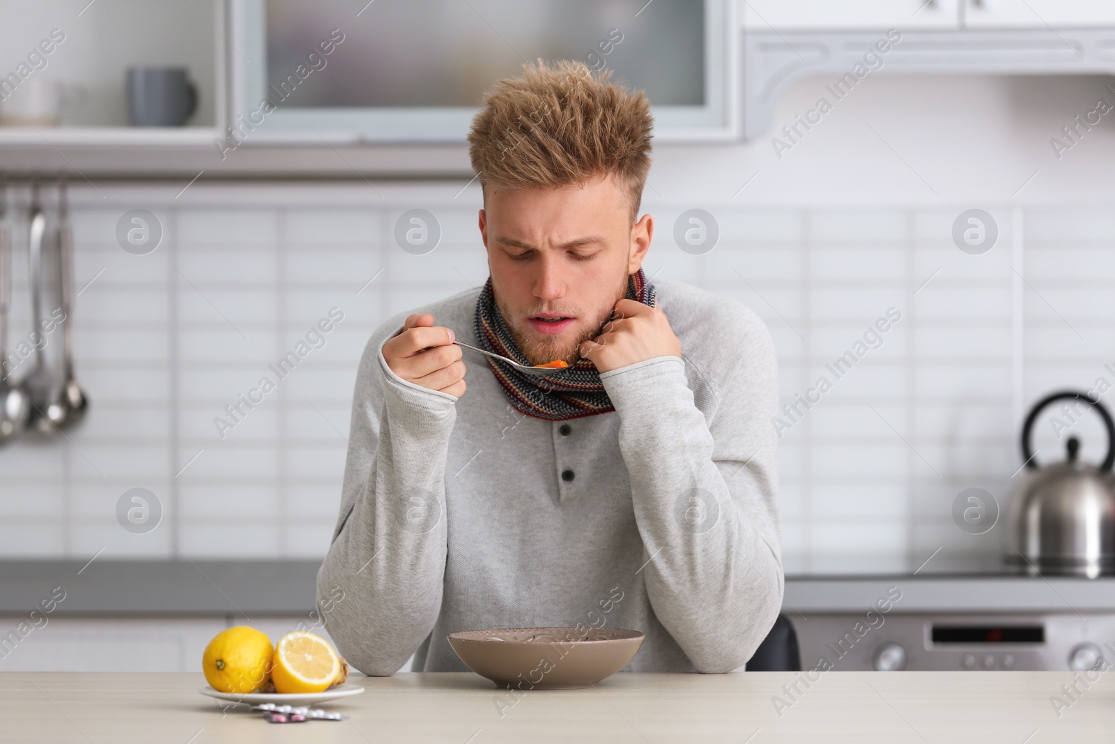 Photo of Sick young man eating soup to cure flu at table in kitchen