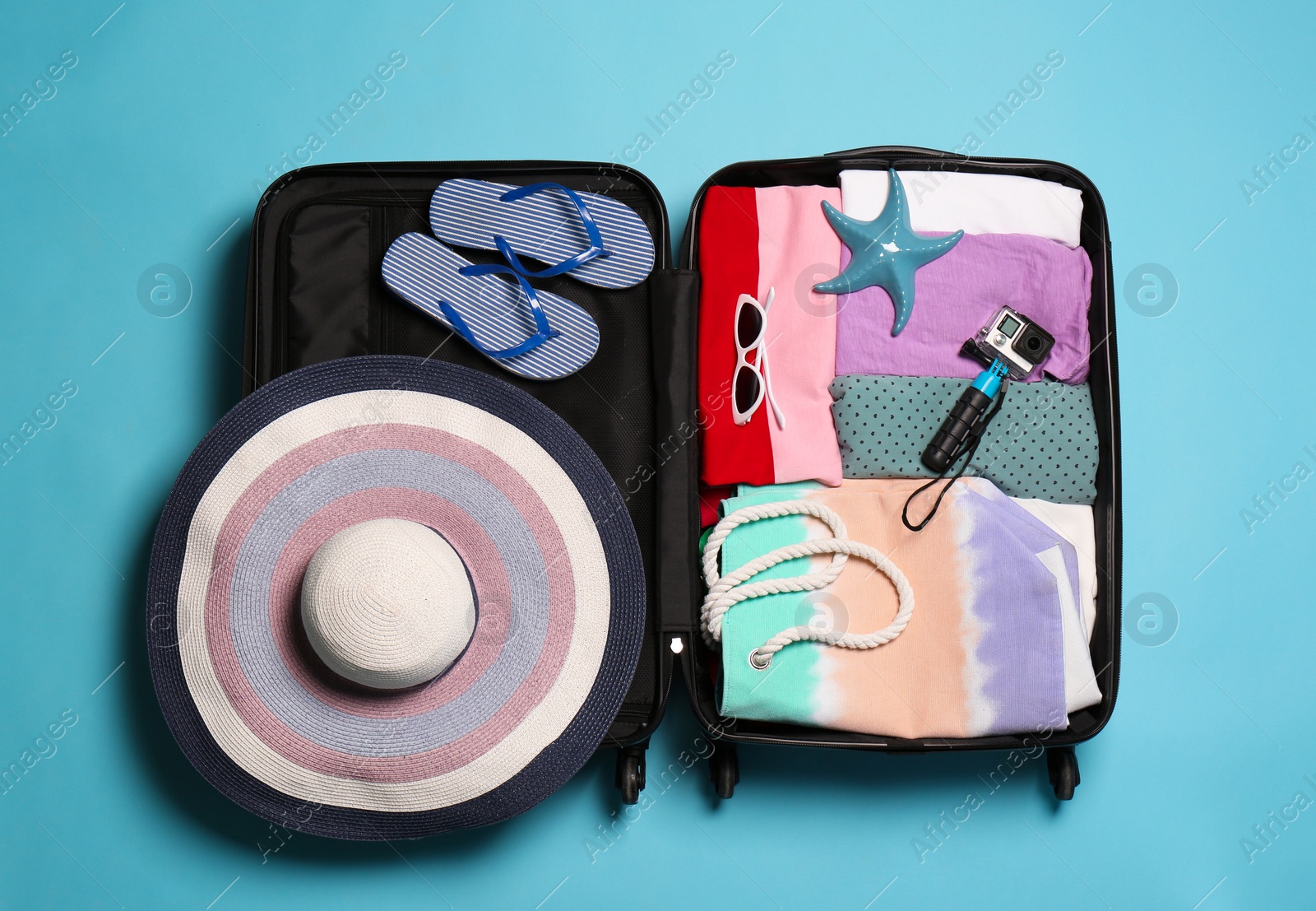 Photo of Open suitcase with traveler's belongings on color background, top view