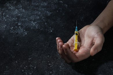 Drug addiction. Man with syringe on black textured table, closeup and space for text
